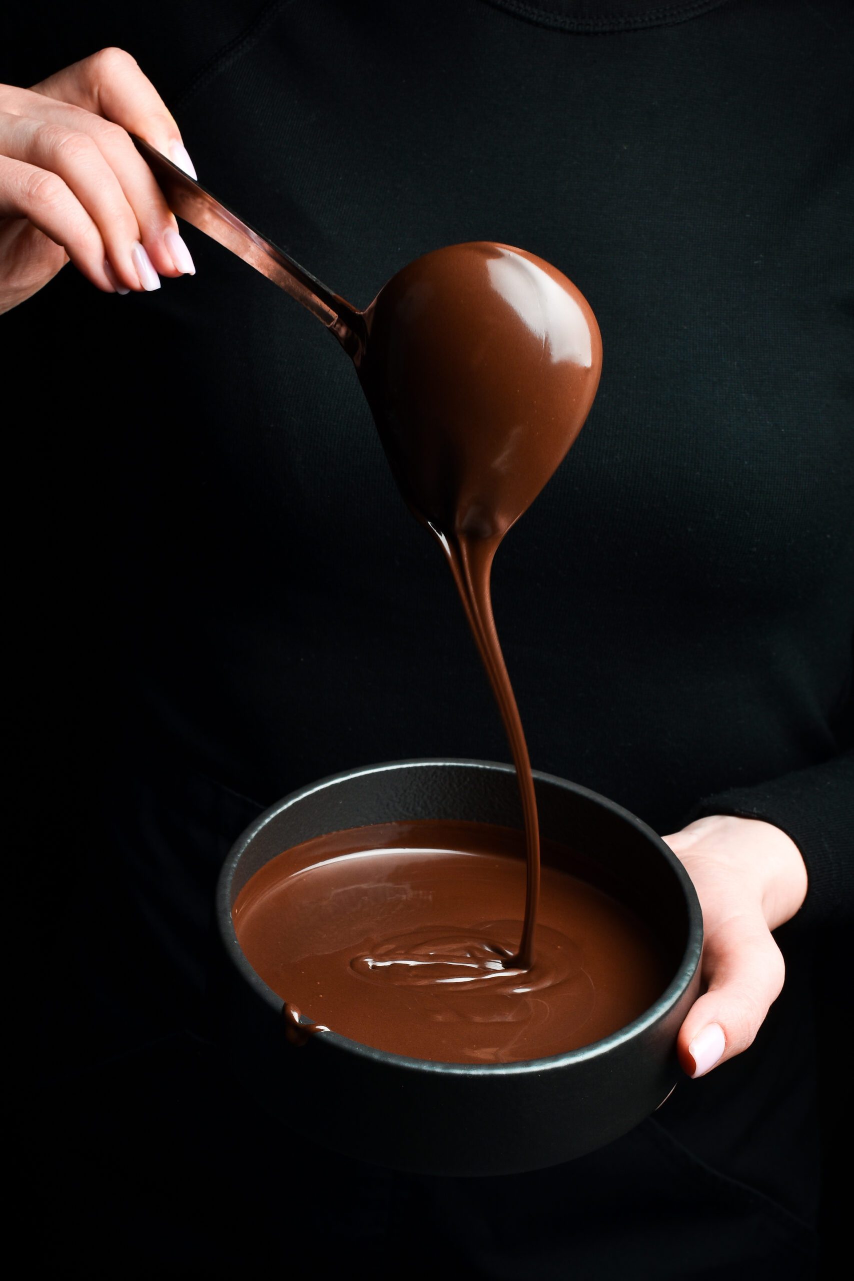 The chef scoops hot chocolate into a bowl. On a black background. Preparation of chocolate.